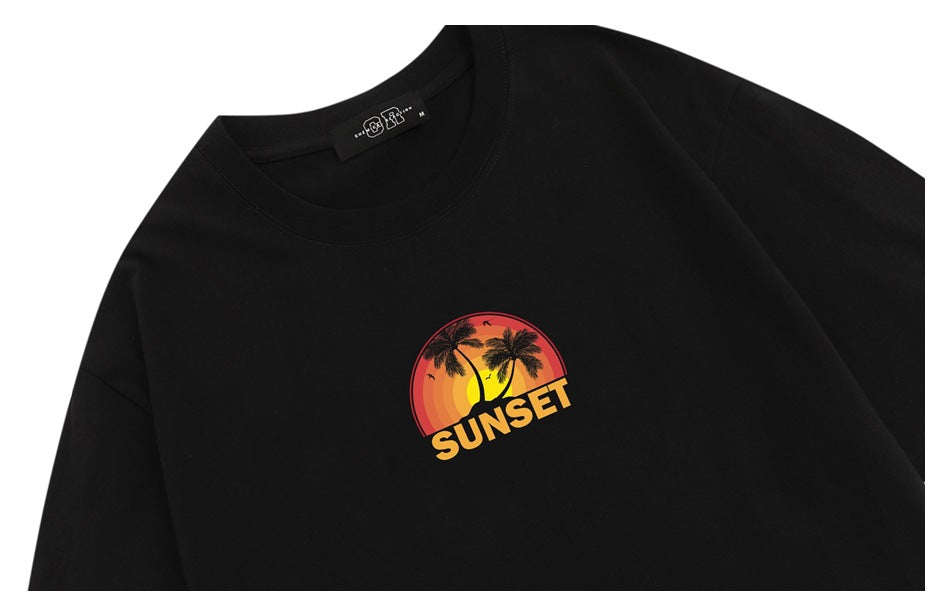 Close-up of a black T-shirt front with a colorful sunset and palm tree graphic reading “SUNSET.”
