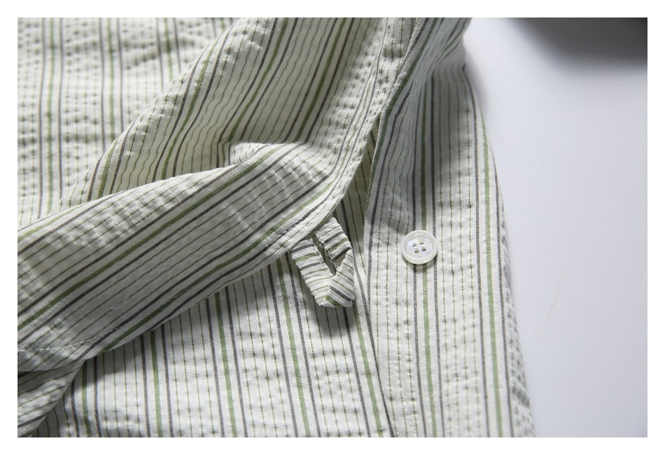 Close-up of a white shirt with narrow green and gray stripes, showing a button and folded cuff area.