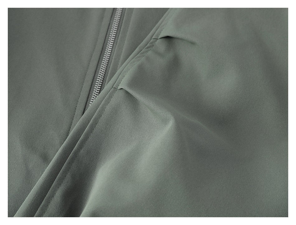 Close-up of a muted gray-green garment showing a metal zipper and a stitched pocket opening.