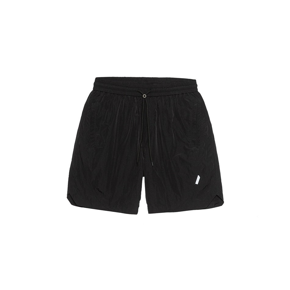 Black drawstring shorts with crinkled finish, elastic waistband, side pockets and small white tab, flat front view