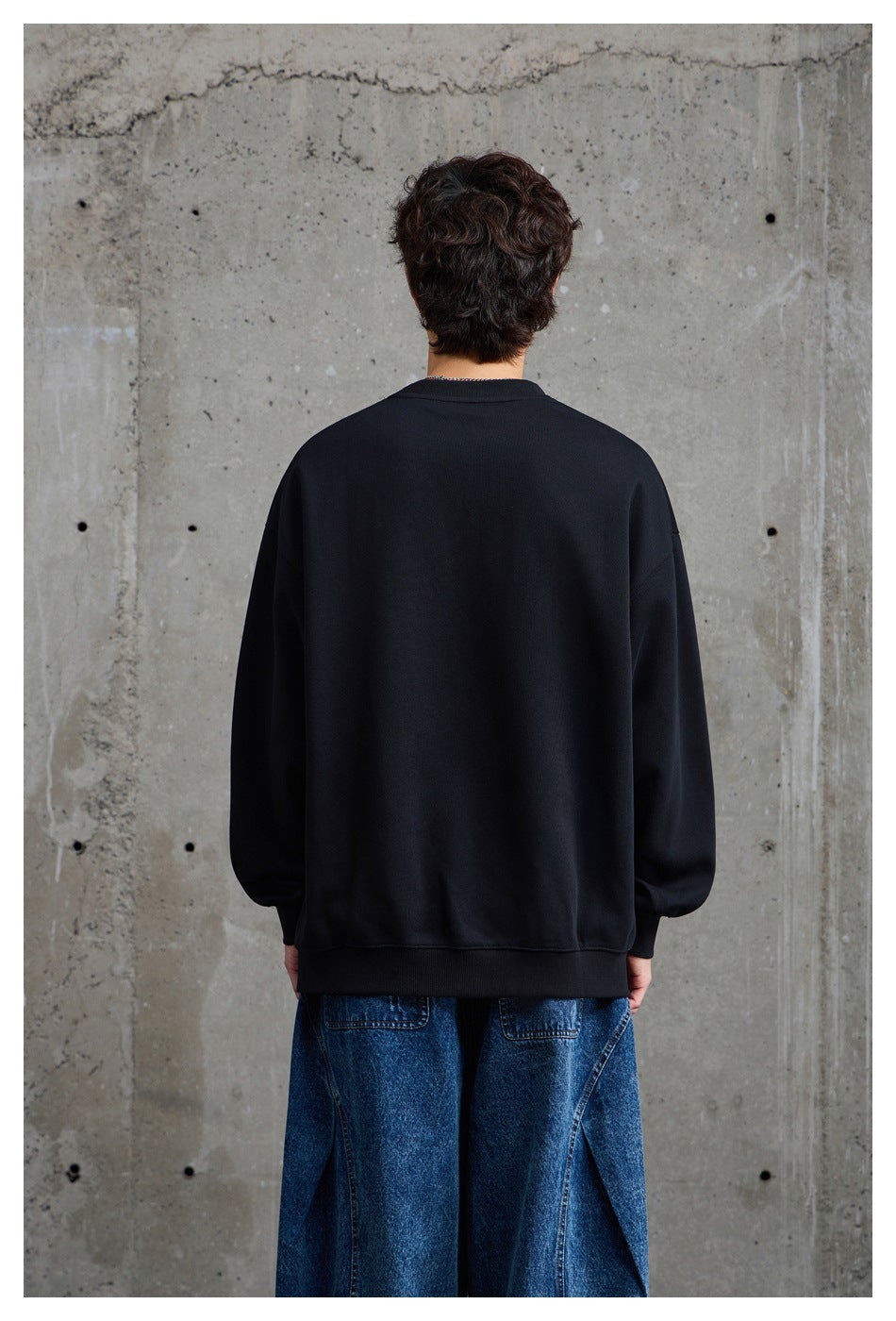 Back view of a model wearing a plain black oversized crewneck sweatshirt with ribbed cuffs and hem.