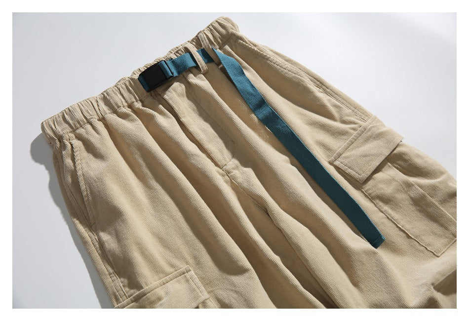 Angled overhead view of beige cargo pants with an elastic waist, teal belt strap and black buckle, and large flap pockets.