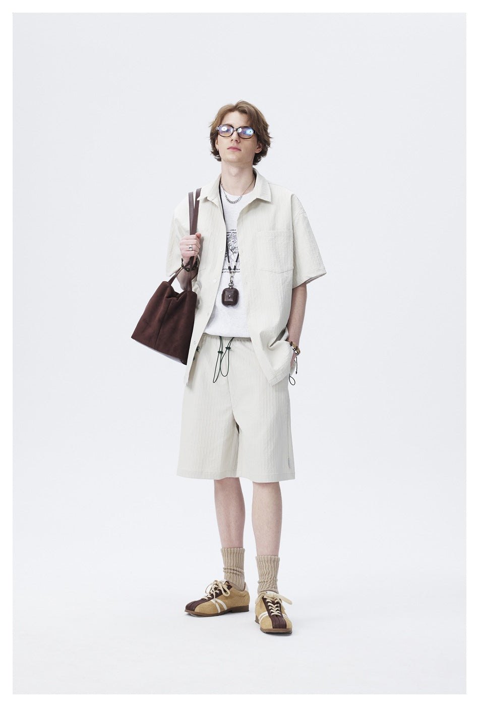 Model wearing the light textured short-sleeve shirt open over a white tee with matching shorts and a brown bag