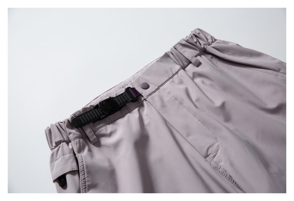 Close-up of mauve-gray pants showing the gathered waistband, belt loops, button, and black adjustable buckle strap.
