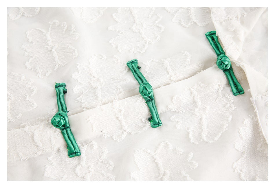 Close-up of three green frog closures on a white shirt with a raised floral pattern.