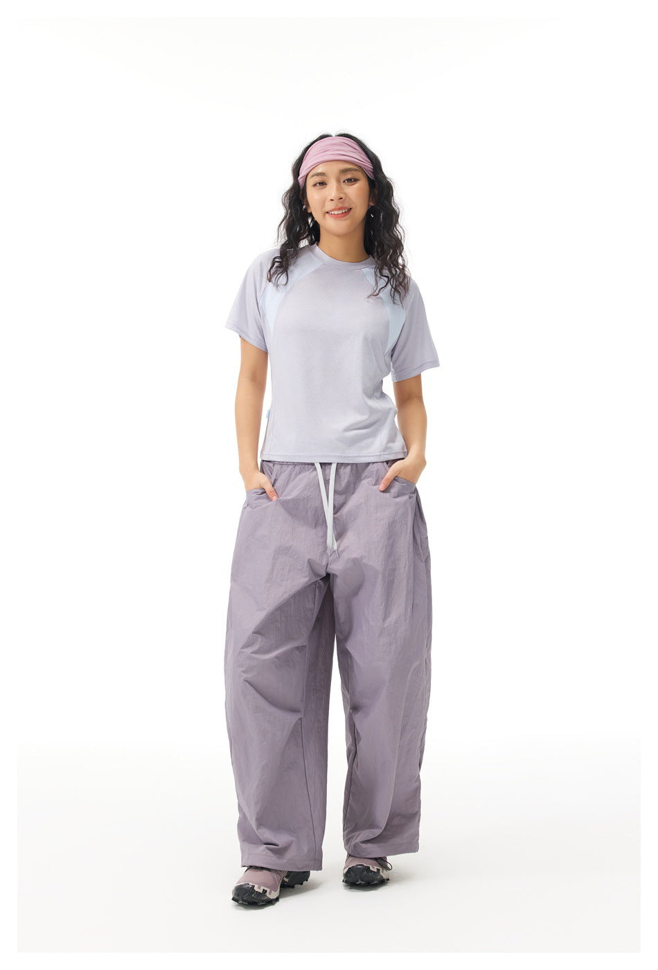 Model wearing a pale lavender color-block T-shirt and loose lavender-gray drawstring pants with hands in pockets.