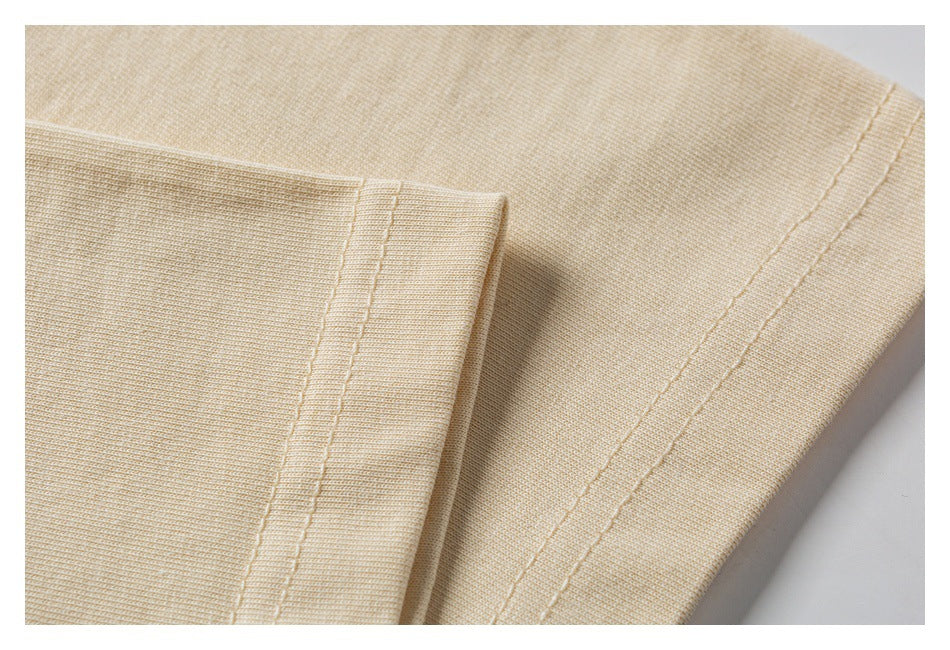 Close-up of cream-colored knit garment fabric with parallel stitching along a folded edge.
