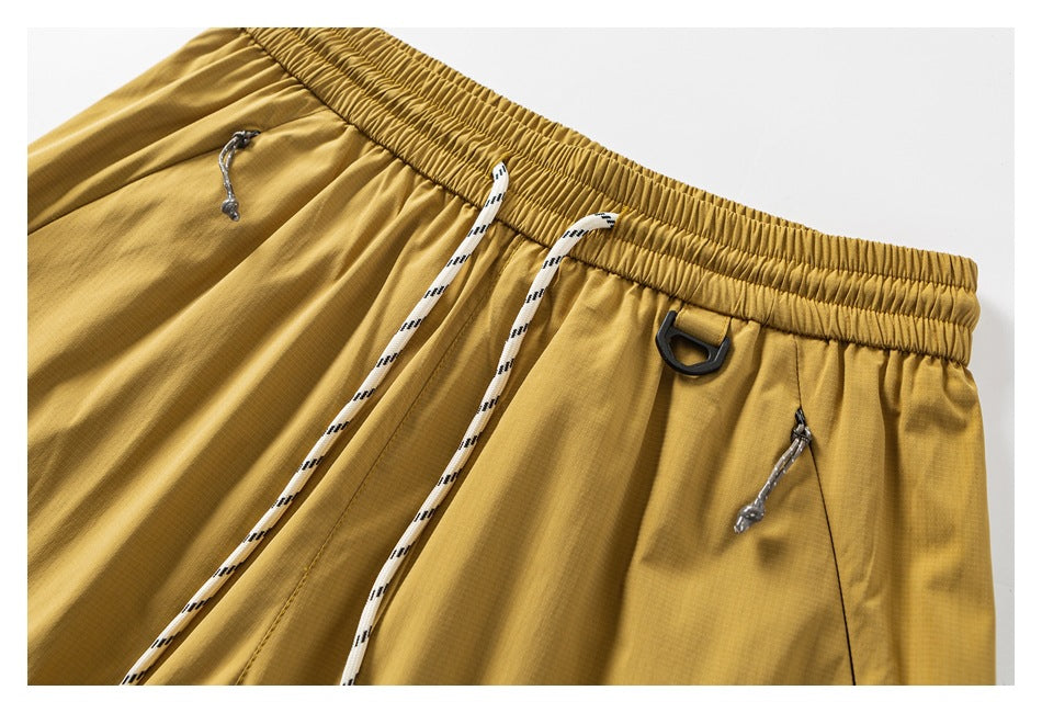 Close-up of mustard pants showing the elastic drawstring waist, front zip pockets, and a black loop.