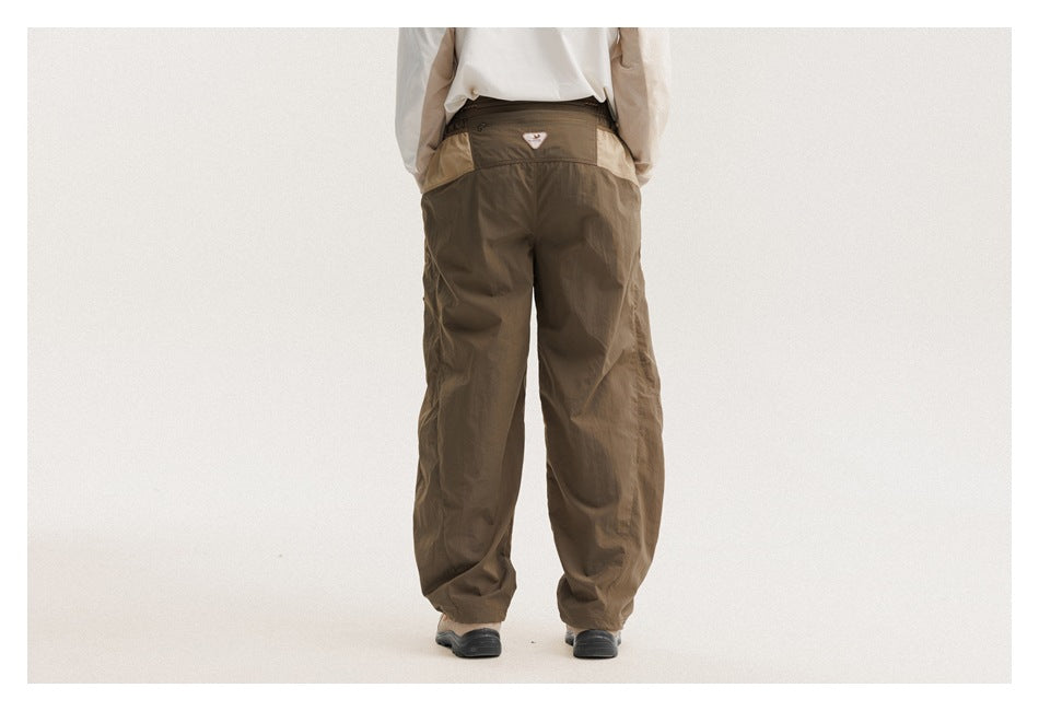 Back view of a model wearing olive-brown pants with a contrasting tan waistband panel and gathered cuffs.