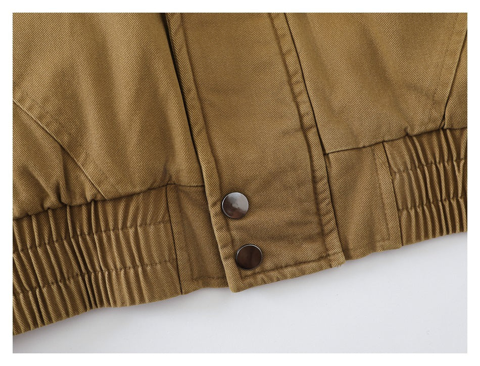 Close-up of a tan jacket hem with gathered elastic and two dark snap buttons.