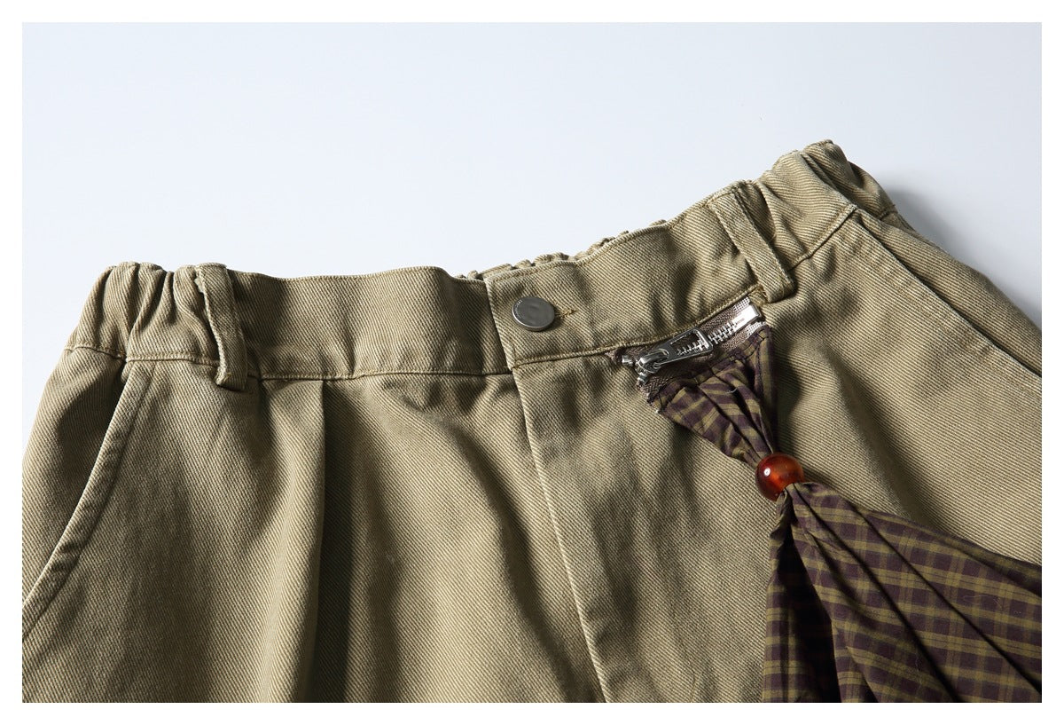 Close-up of the khaki shorts' front waistband, button, zipper, and plaid accent with an amber bead.