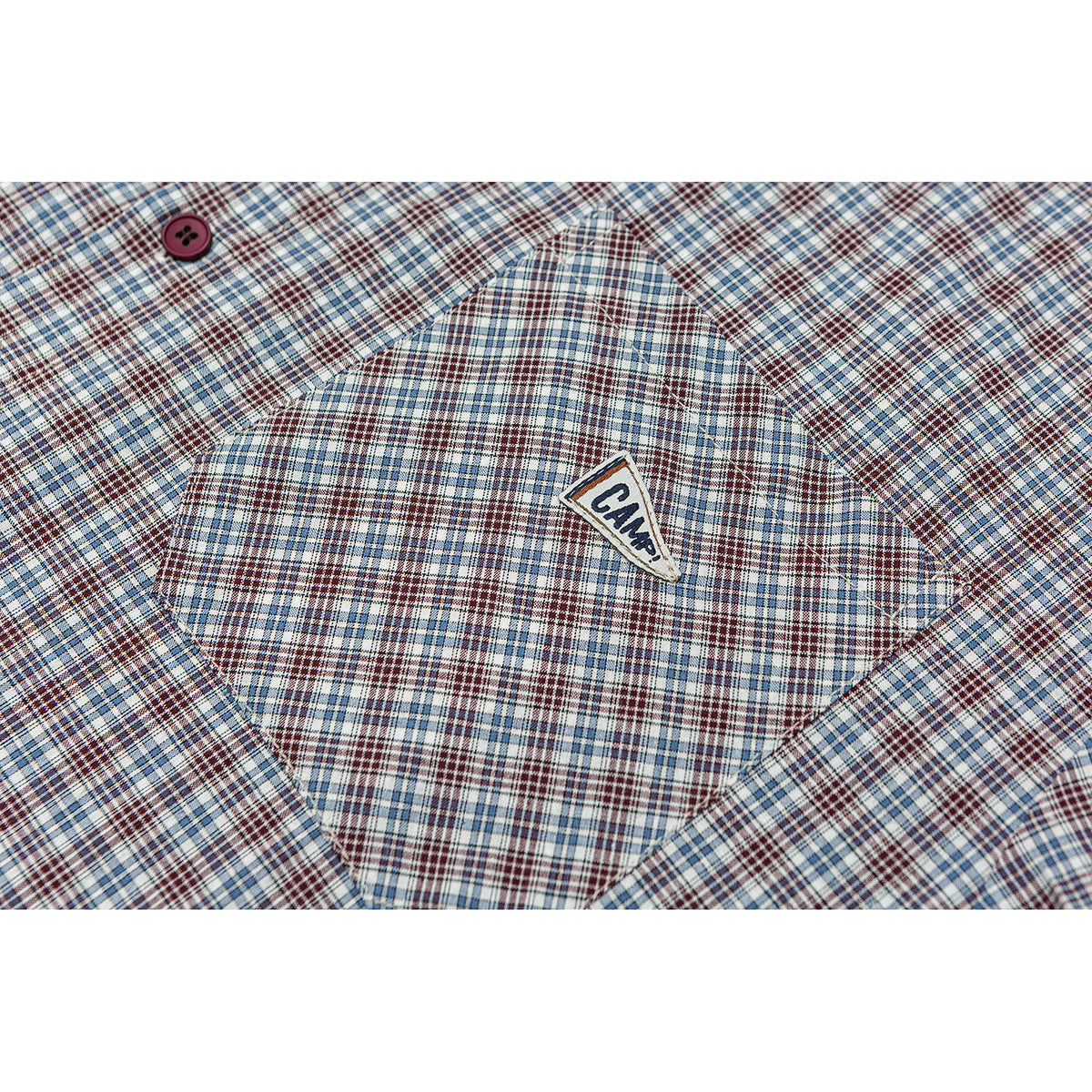 Close-up of a plaid shirt pocket with a small triangular sewn-on patch and a burgundy button.