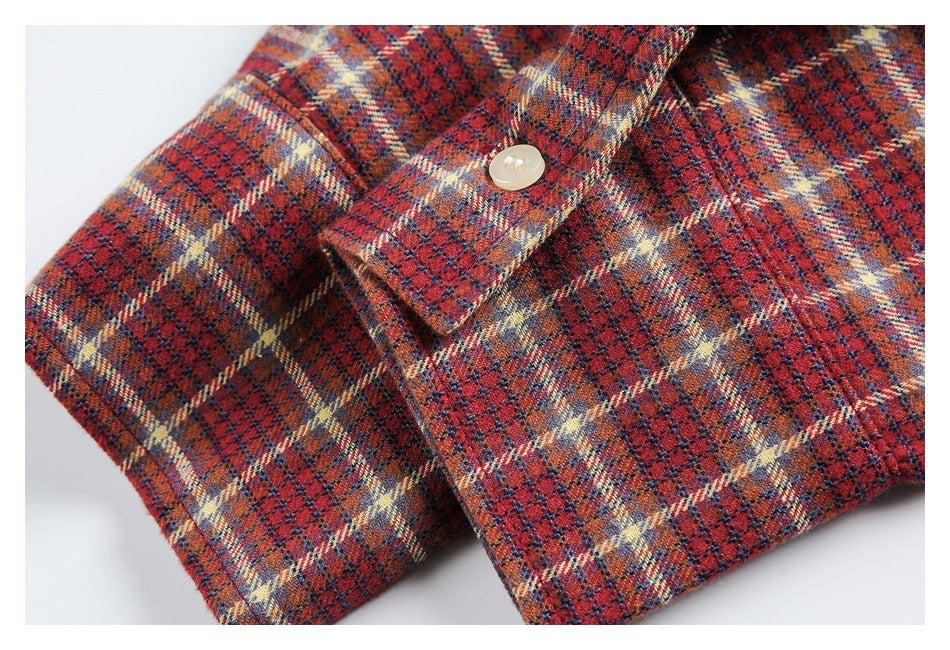 Close-up of a cream button and folded cuff on a red, navy, and cream plaid shirt.
