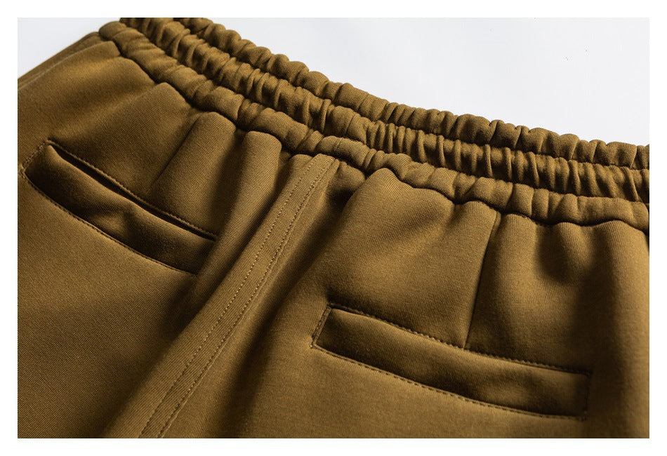 Close-up of olive-brown pants showing an elastic waistband, front fly, and two slanted pockets.