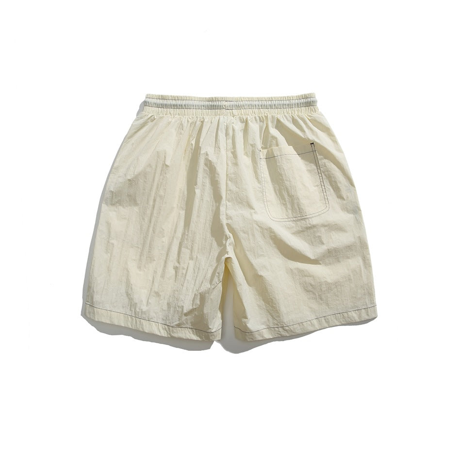 Cream shorts shown from the back, with an elastic waistband, a single patch pocket, and stitched hems.