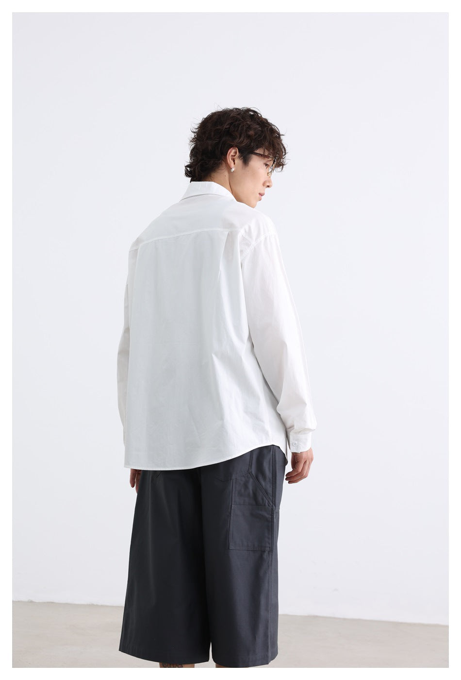 Rear view of a model wearing a white button-down shirt and charcoal knee-length shorts.
