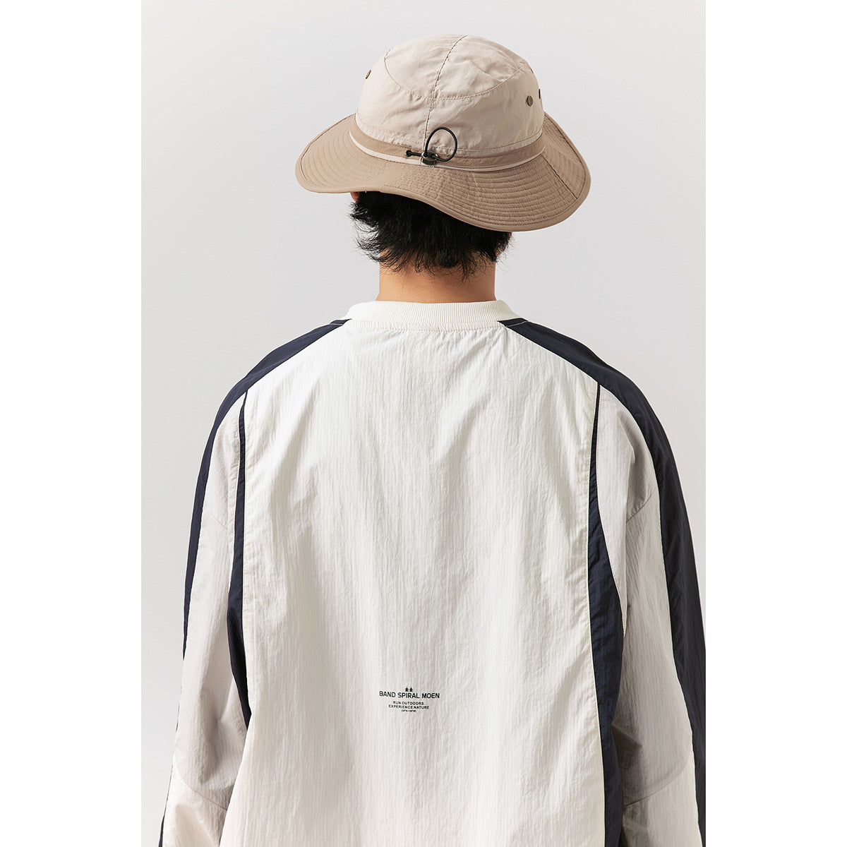 Rear close-up of a model wearing an ivory pullover with navy sleeve panels and small printed text near the lower back.