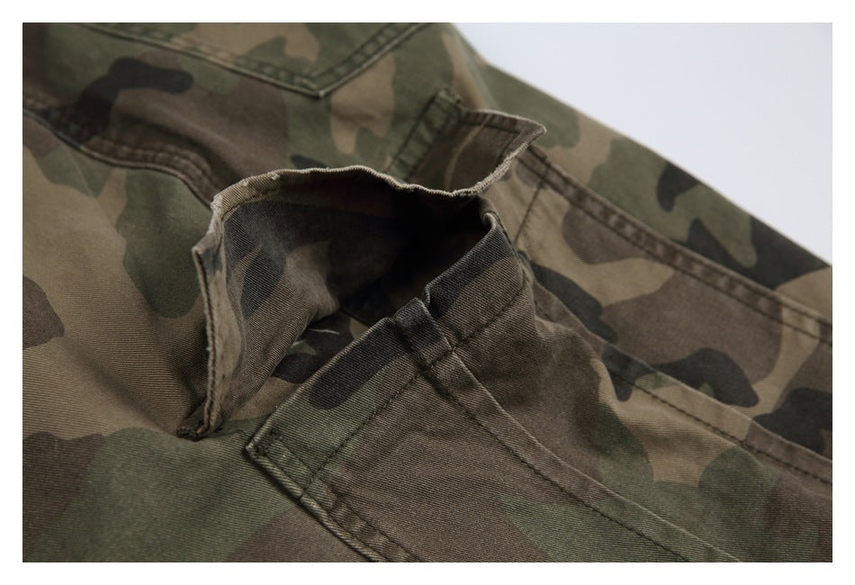 Close-up of camouflage trousers showing the waistband, belt loop, and stitched pocket construction.