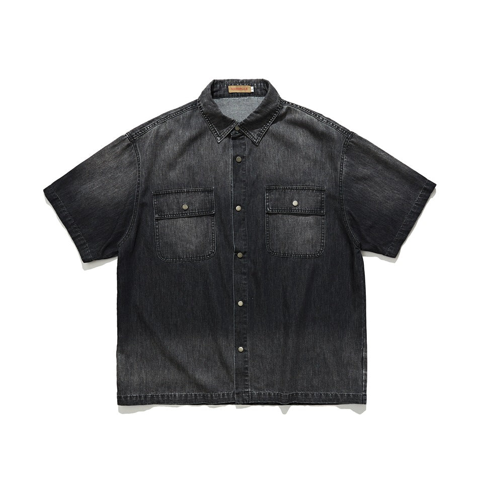 Front view of a black denim short-sleeve button-up shirt with a pointed collar and two flap chest pockets.