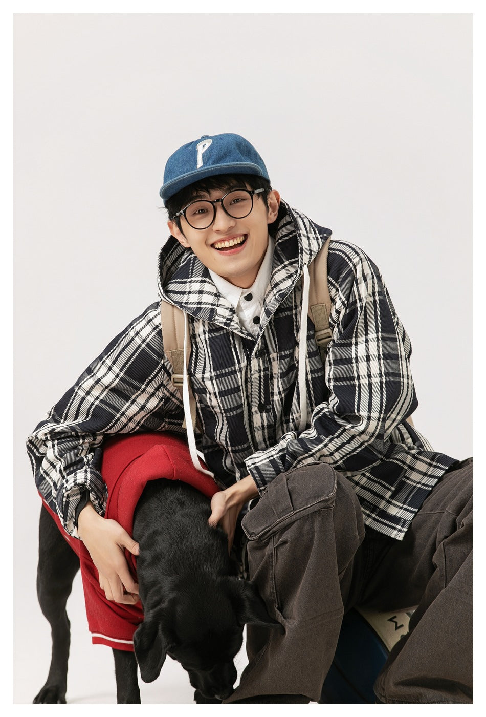 Model wearing a black-and-white plaid hooded button coat while seated beside a black dog.