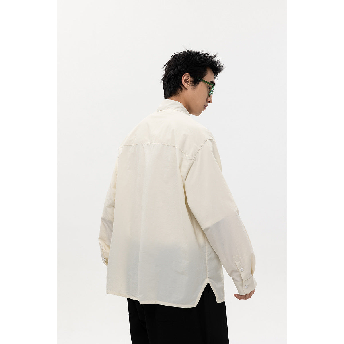 Rear view of a model wearing an oversized ivory shirt with a back yoke and side hem slit.