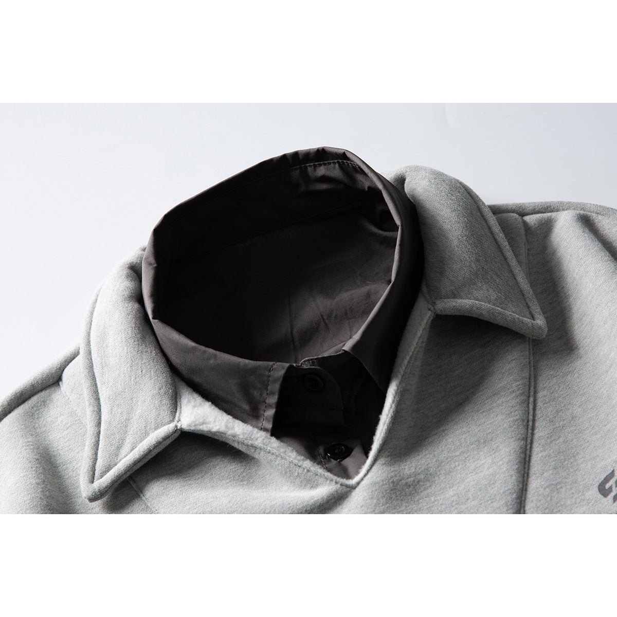 Close-up of a light gray sweatshirt's pointed collar layered over a black button-up shirt.
