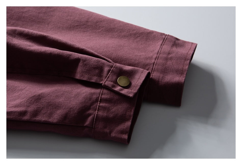 Close-up of a burgundy sleeve cuff with a brass-colored button and stitched edges.