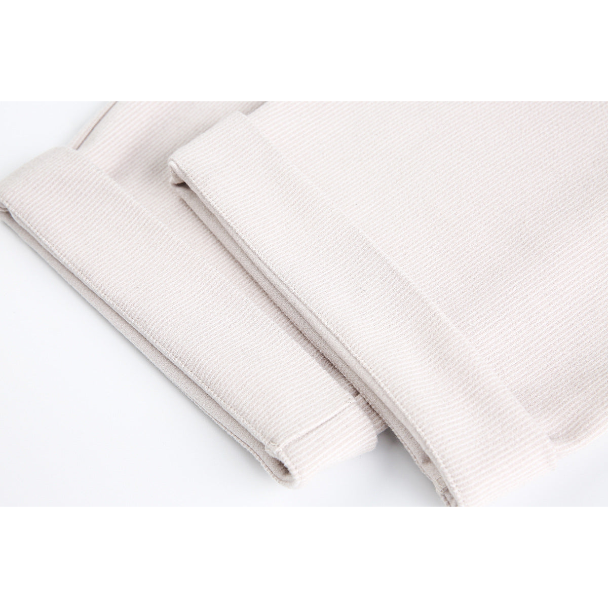 Close-up of folded ivory trouser legs showing the fine fabric texture and stitched edges.