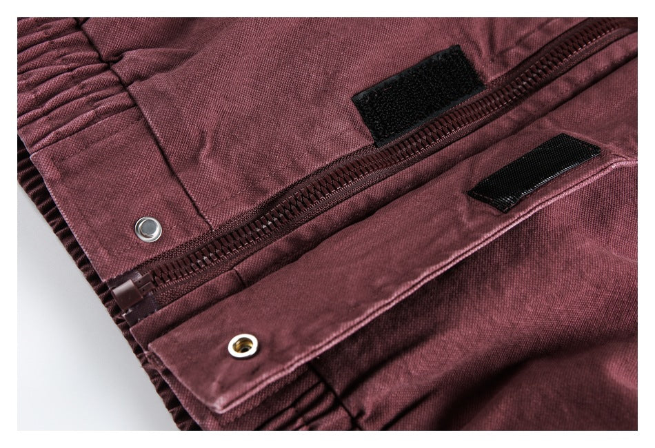 Close-up of a burgundy garment's zipper, hook-and-loop tabs, and metal eyelets.