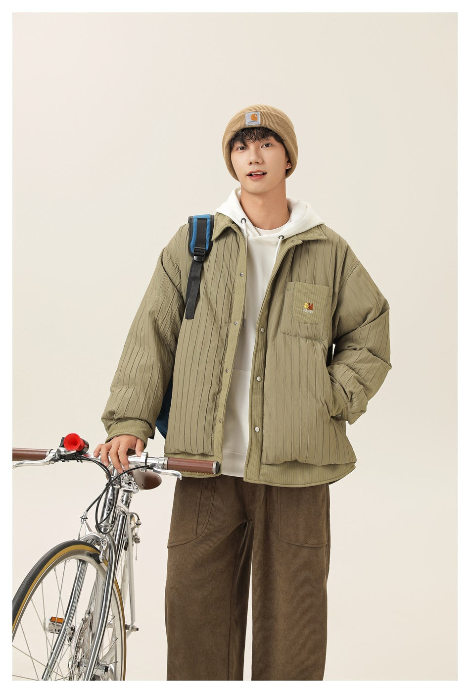 A model wears an olive quilted button-front jacket with a chest pocket over a white hoodie.