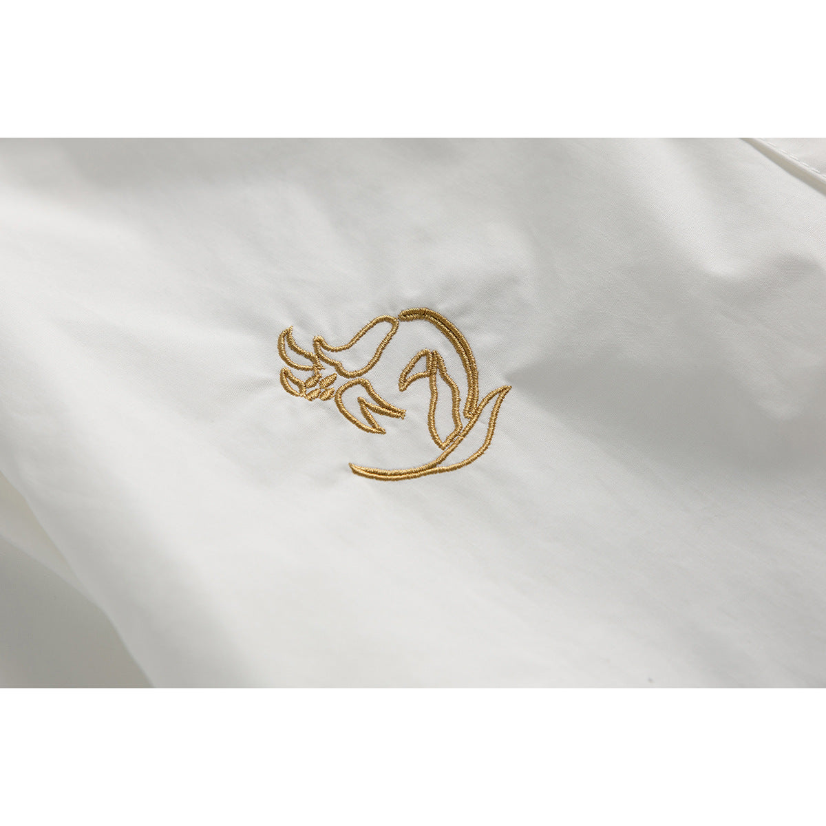 Close-up of gold line-art embroidery on white shirt fabric.