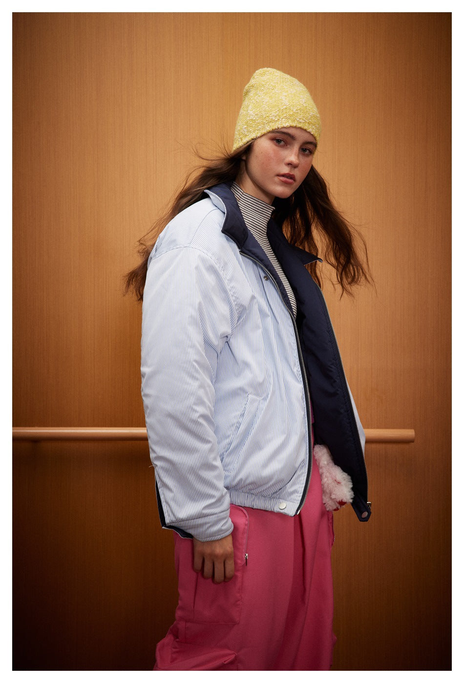Model in a light blue pinstriped jacket with navy lining, shown at an angle with pink cargo trousers.