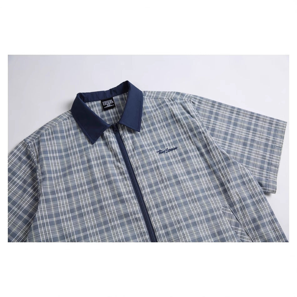 Blue-gray plaid short-sleeve zip-up shirt laid flat, with a navy collar and small chest embroidery.