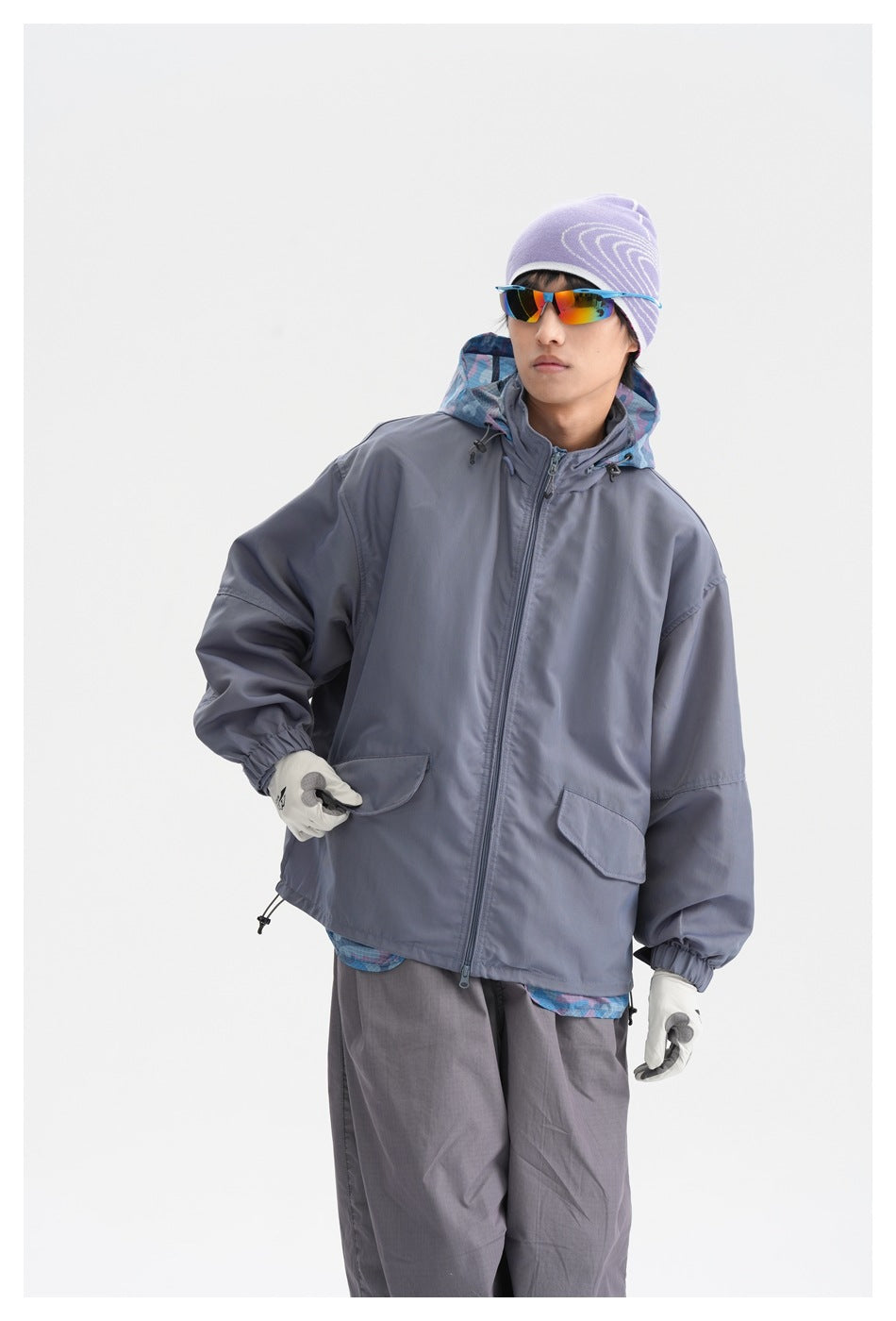 Model wearing a zip-front slate gray hooded jacket with flap pockets and blue patterned lining, shown from the front.