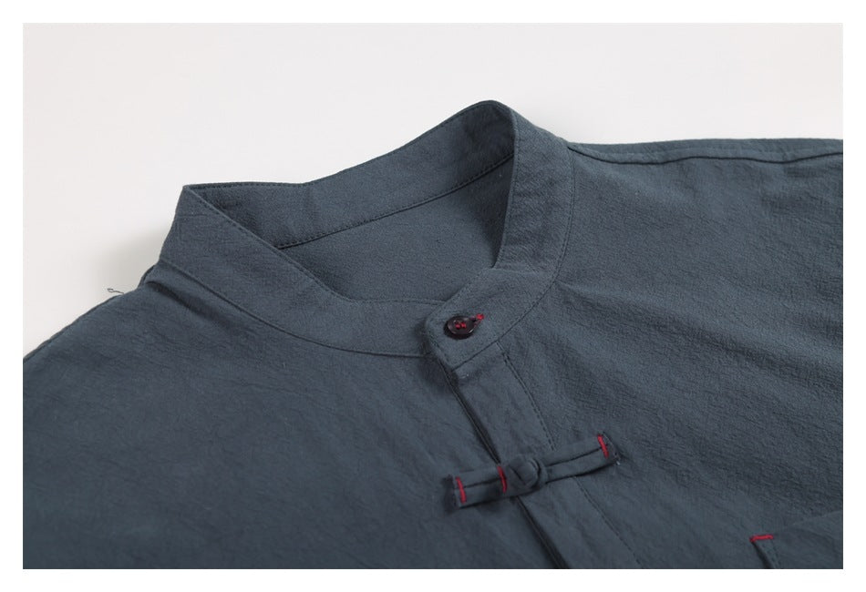 Close-up of a slate-blue shirt's stand collar, button, and frog closure with red stitching.