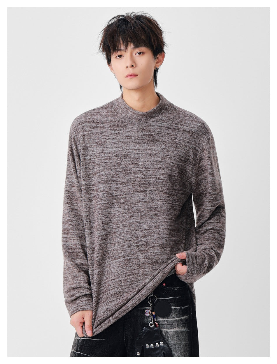 Model wearing a taupe-gray marled long-sleeve top and holding its hem to show the fit.