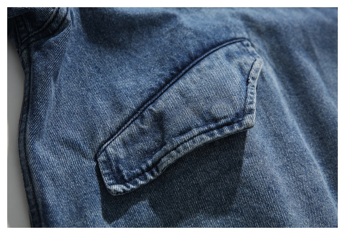 Close-up of a flap pocket on faded blue denim, showing stitching and a metal snap.