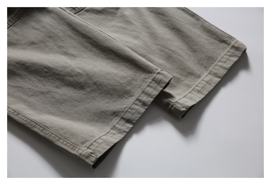 Close-up of the stitched hem and folded edge of taupe-gray trousers.