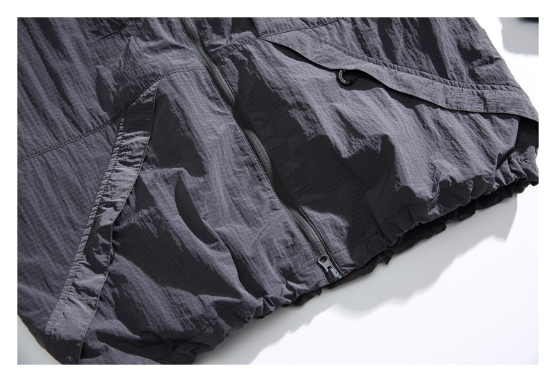 Close-up of a charcoal gray jacket hem with a gathered edge, seam, and zip pocket.