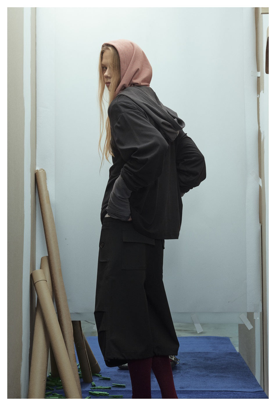 Side and partial back view of a model wearing a black top with a red striped hood and gray striped hood layer.