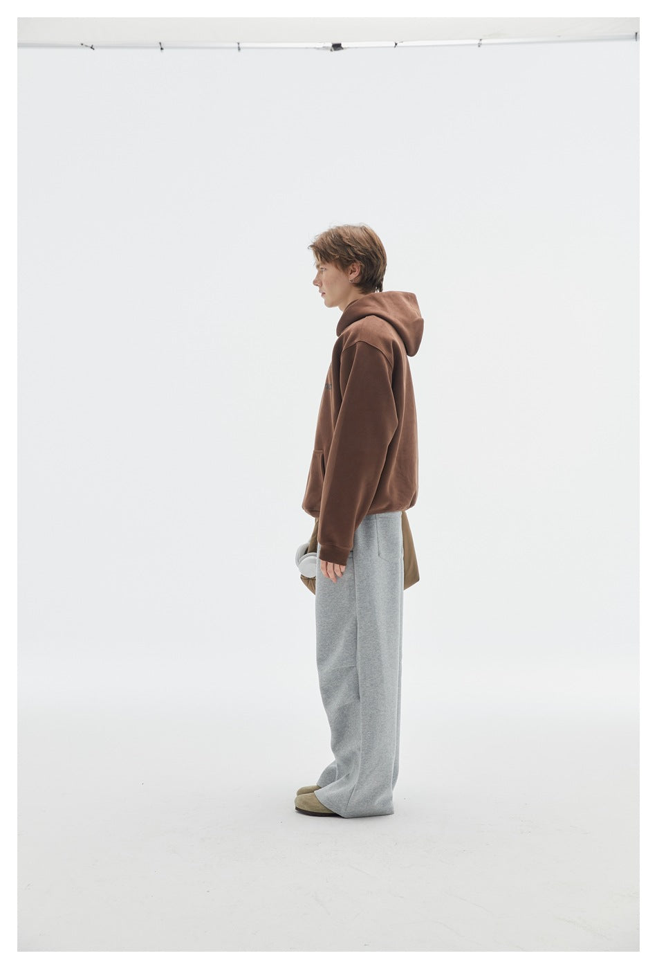 Side view of model wearing heather gray wide-leg sweatpants with a brown hoodie and tan suede shoes