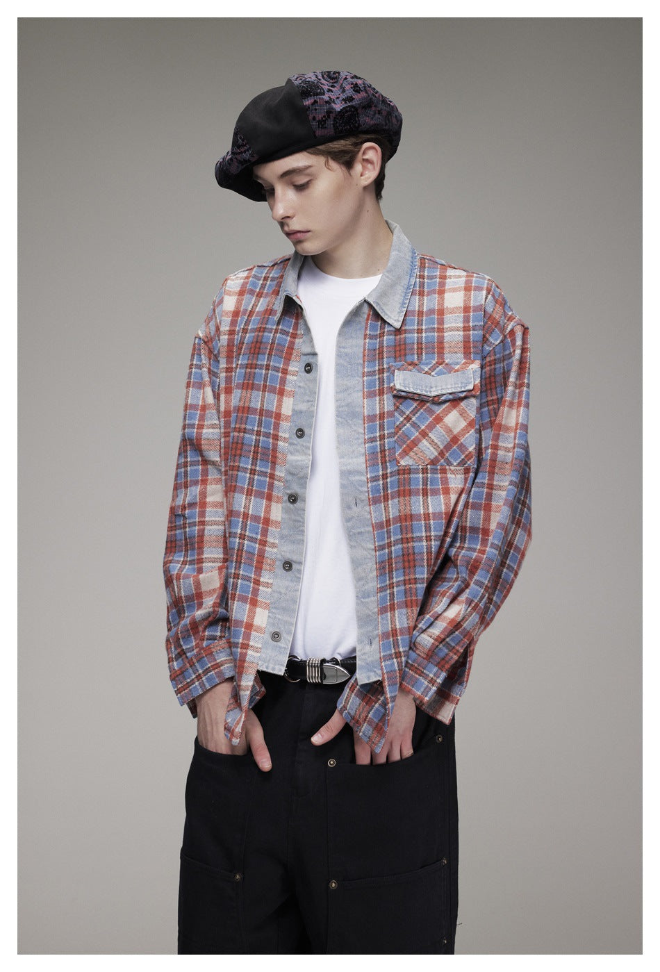 Model looking down wearing the plaid shirt open over a white tee with black pants and a beret, showing the chest pocket