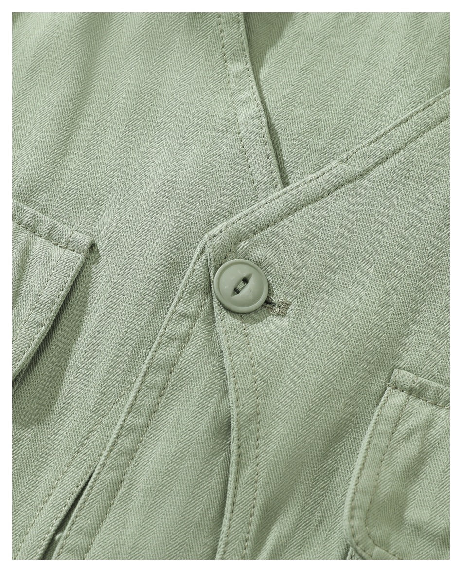 Close-up of sage-green herringbone fabric, a button, and stitched garment seams.