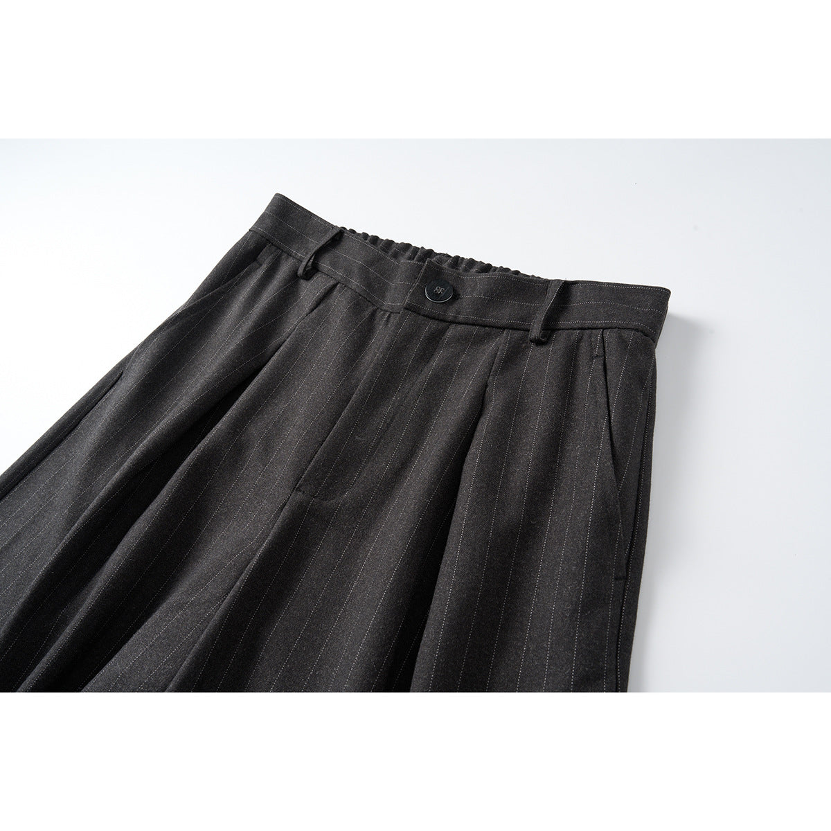 Angled close view of charcoal pinstripe wide-leg trousers, showing the buttoned waistband, belt loops, pleats and side