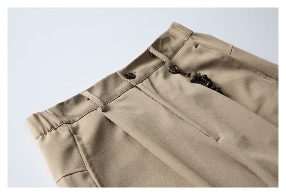 Close-up of beige trousers showing the waistband, belt loops, button, and decorative cord detail.