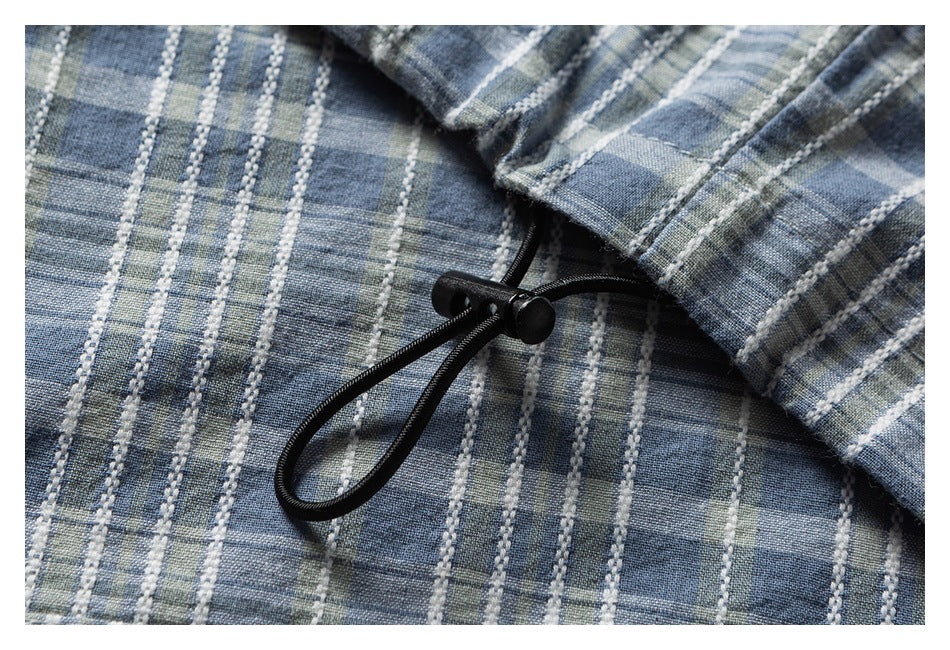 Close-up of blue-gray plaid fabric with a black drawcord and toggle.