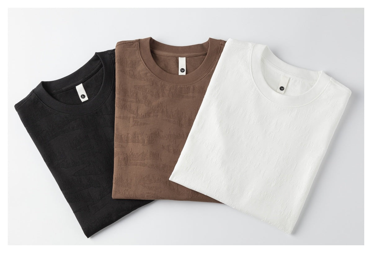 Three folded textured crew-neck T-shirts in black, brown and white laid side by side