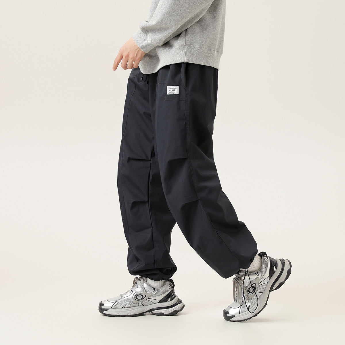 Model wearing loose black pants with panel seams and a small thigh patch, shown from the front at an angle.
