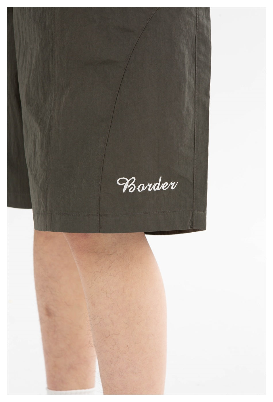 Close-up of olive shorts hem with curved panel seam and white script embroidery on a model's leg