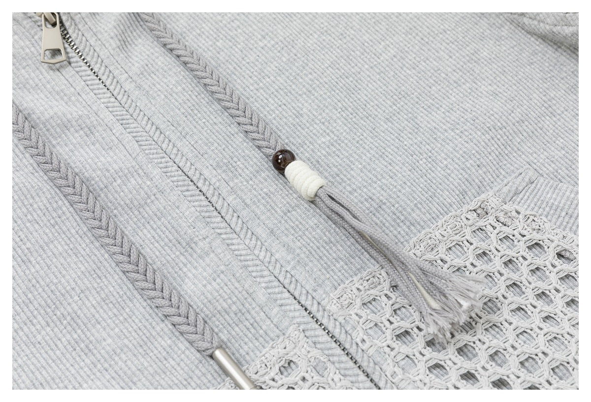 Close-up of a light gray ribbed knit top with a zipper, cord detail, and openwork crochet panel.